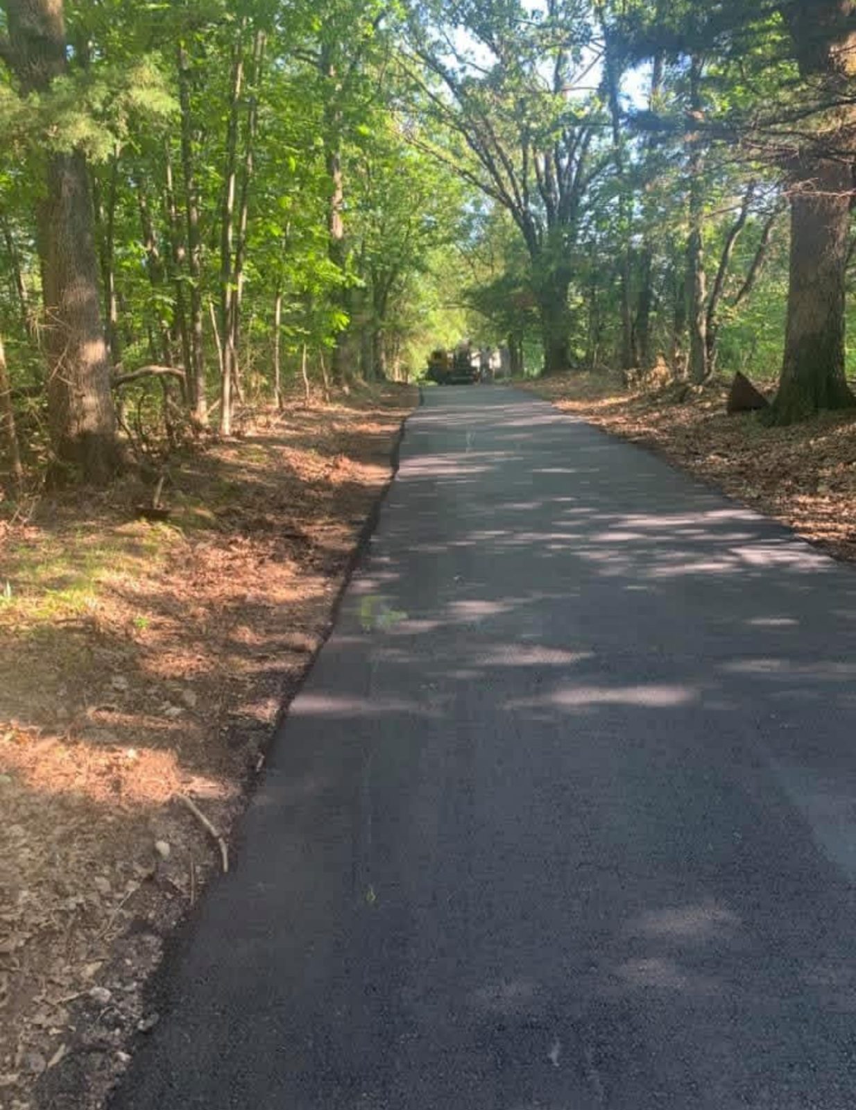 Newly paved asphalt access lane through a wooded property